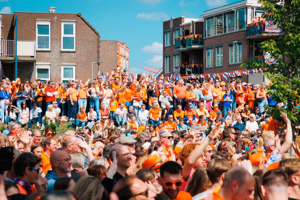 Mensen in oranje kleding zwaaien mee tijdens optreden