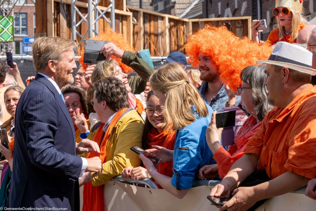 Willem-Alexander glimlacht naar man met oranje pruik in publiek