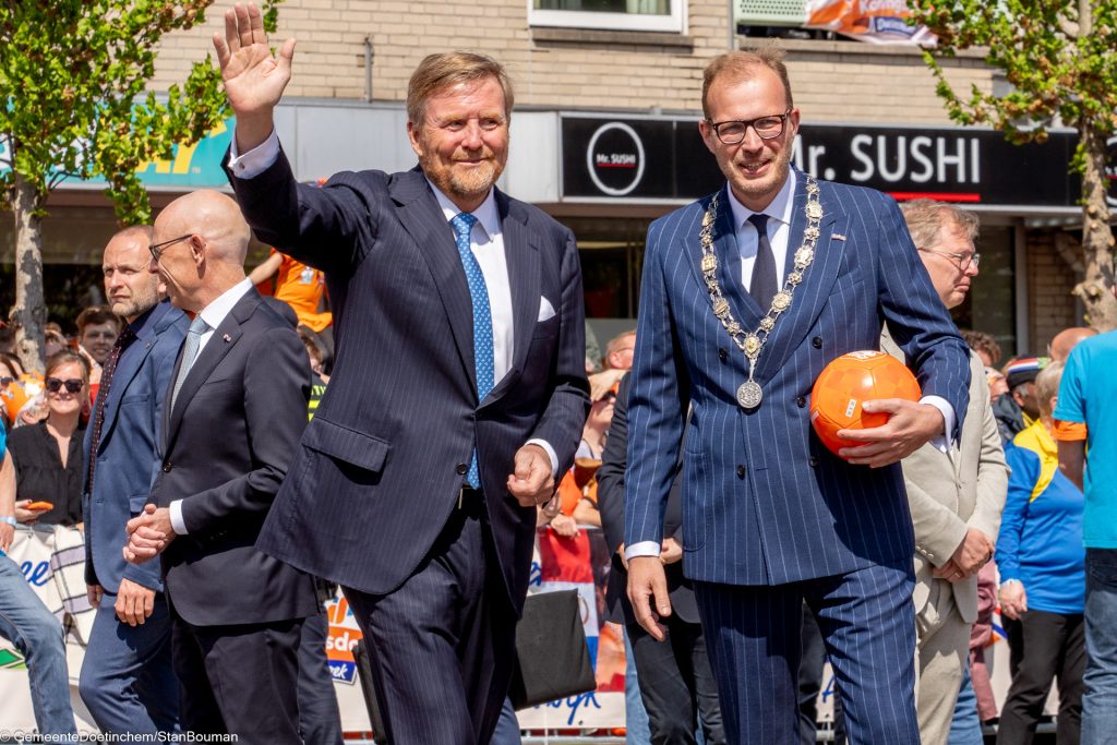 Koning Willem-Alexander zwaait naar publiek en burgemeester Mark Boumans houdt oranje bal vast