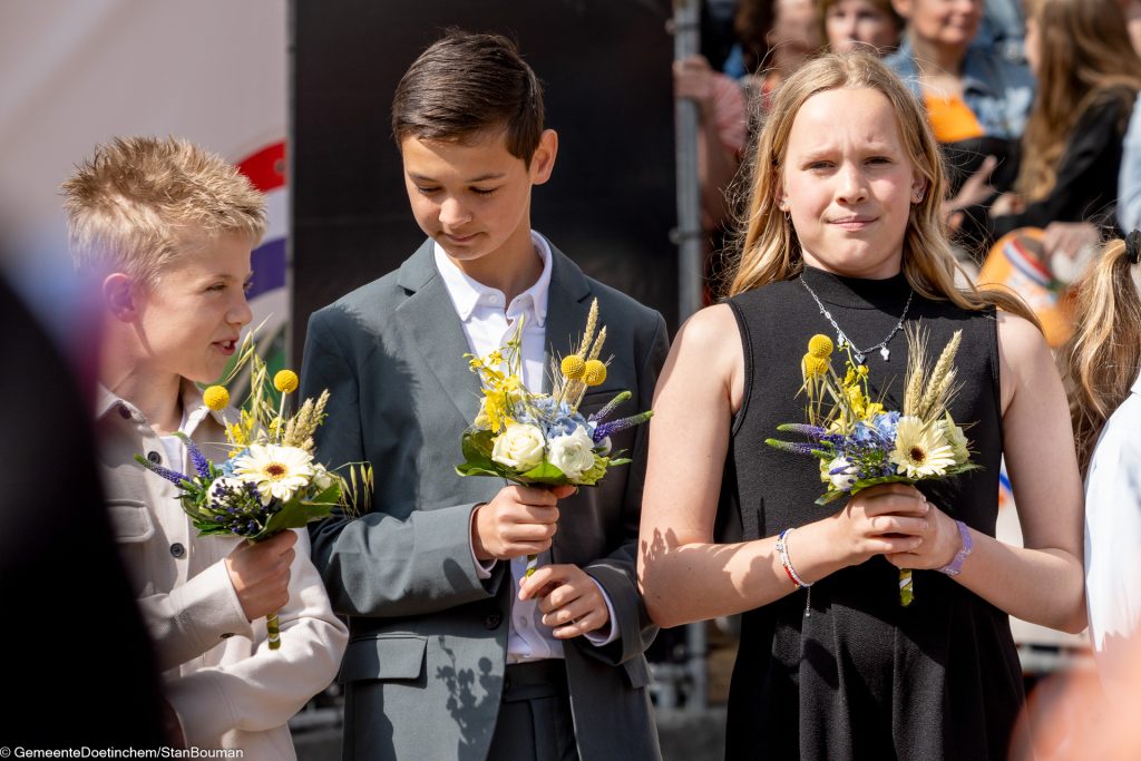 Kinderen wachten op koninklijk paar met bloemstukken
