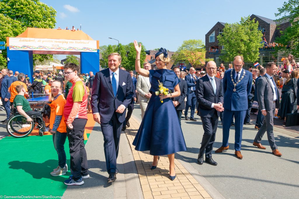 Koningin Maxima zwaaiend naar publiek, naast Willem-Alexander
